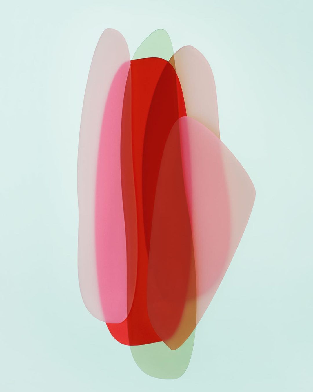 Abstract art featuring overlapping translucent shapes in shades of red, pink, and green against a pale blue background, creating a soft, layered effect.