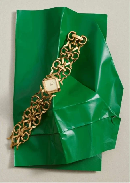 Gold chain-link watch displayed on folded shiny green material; fashion accessory, jewellery and modern presentation.