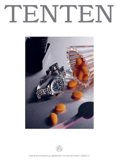 Close-up product shot of a wristwatch alongside a glass jar with orange pills and a spoon on a silver surface. Minimalist style.