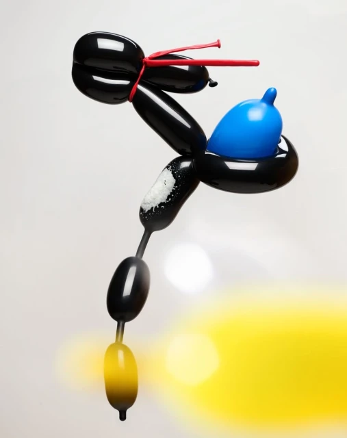 Sculptural balloon animal art against white background; twisted black balloon forming a fantasy creature with blue and red accents.