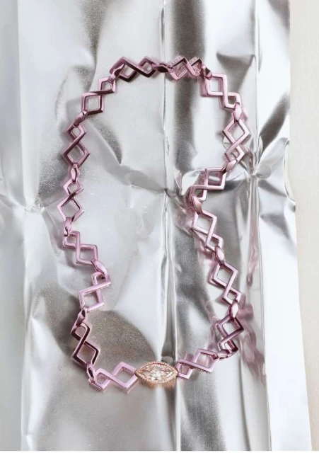 Geometric pink necklace with diamond accent on shimmering silver backdrop. Fashion accessory still life, studio lighting, close-up product shot.
