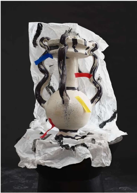 Stylized vase art piece with black paint and color strips, displayed on crumpled white paper with a dark gray background. 