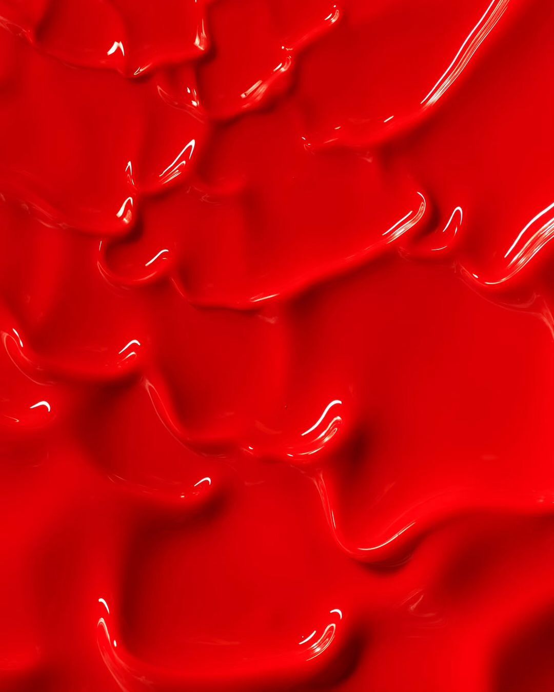 Bright red glossy paint, creating a striking, abstract, textural background; perfect for adding bold color and tactile depth to visuals.