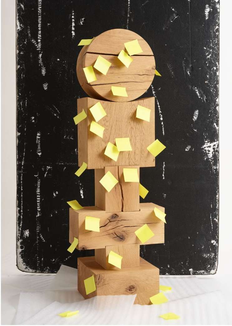 Abstract image of a geometric sculpture made of wood blocks and a wood sphere, with yellow stickers, against a black background.