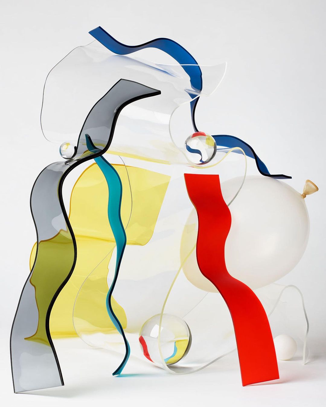 Abstract still life featuring colorful acrylic sheets, clear spheres, and a white balloon against a white background in a studio setting.