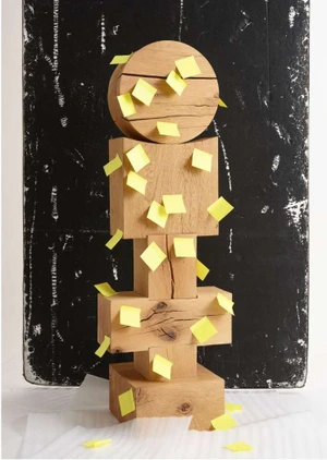Stacked wooden blocks sculpture covered in small yellow sticky notes against a dark textured background