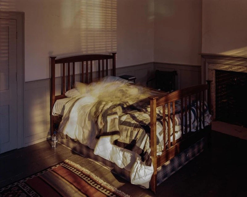 Cozy bedroom interior with a wooden bed, patchwork quilt, soft, diffused light, and a glimpse of a fireplace, creating a warm, inviting atmosphere.