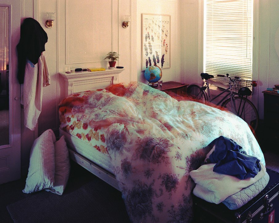 Cozy bedroom scene with a floral patterned bed, vintage bicycle by the window, and soft natural lighting creating a tranquil atmosphere.