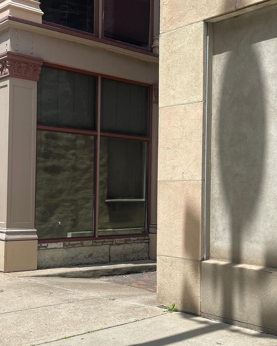 Exterior shot of building corner with large windows and beige stone facade, capturing sunlight and shadows on the sidewalk.