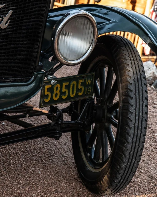 Close-up of a vintage green Ford vehicle showcasing the headlight, tire, and 1919 license plate with the number 58505.