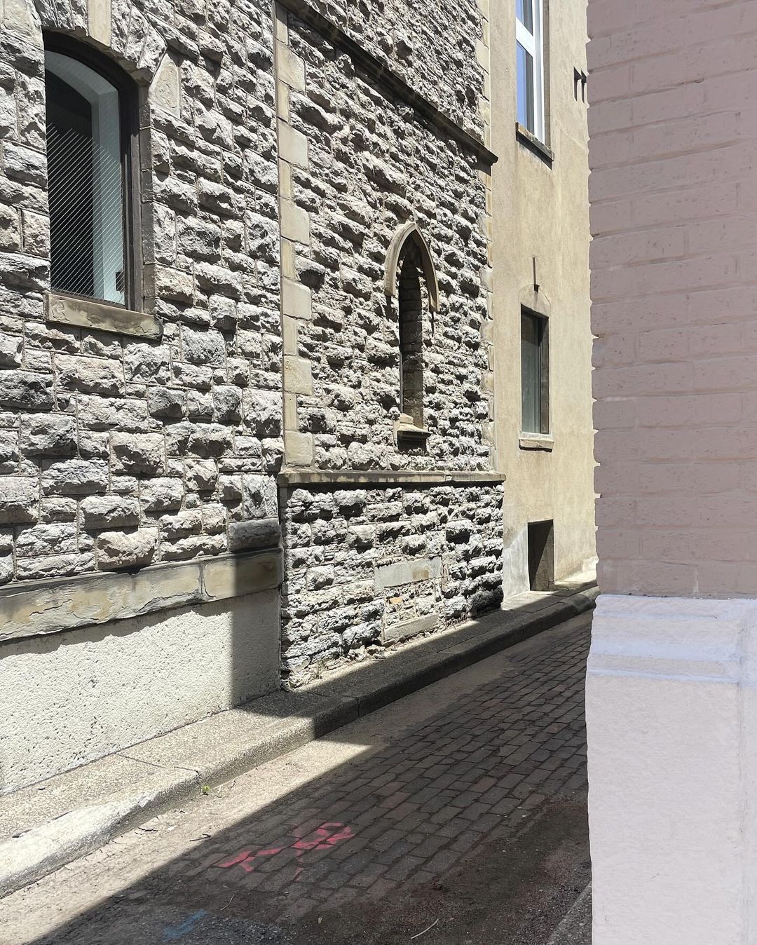 Exterior architectural details of a stone building with window and archway, adjacent to a yellow building, on a cobblestone street.