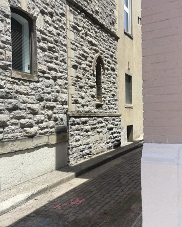 Exterior architectural details of a stone building with window and archway, adjacent to a yellow building, on a cobblestone street.