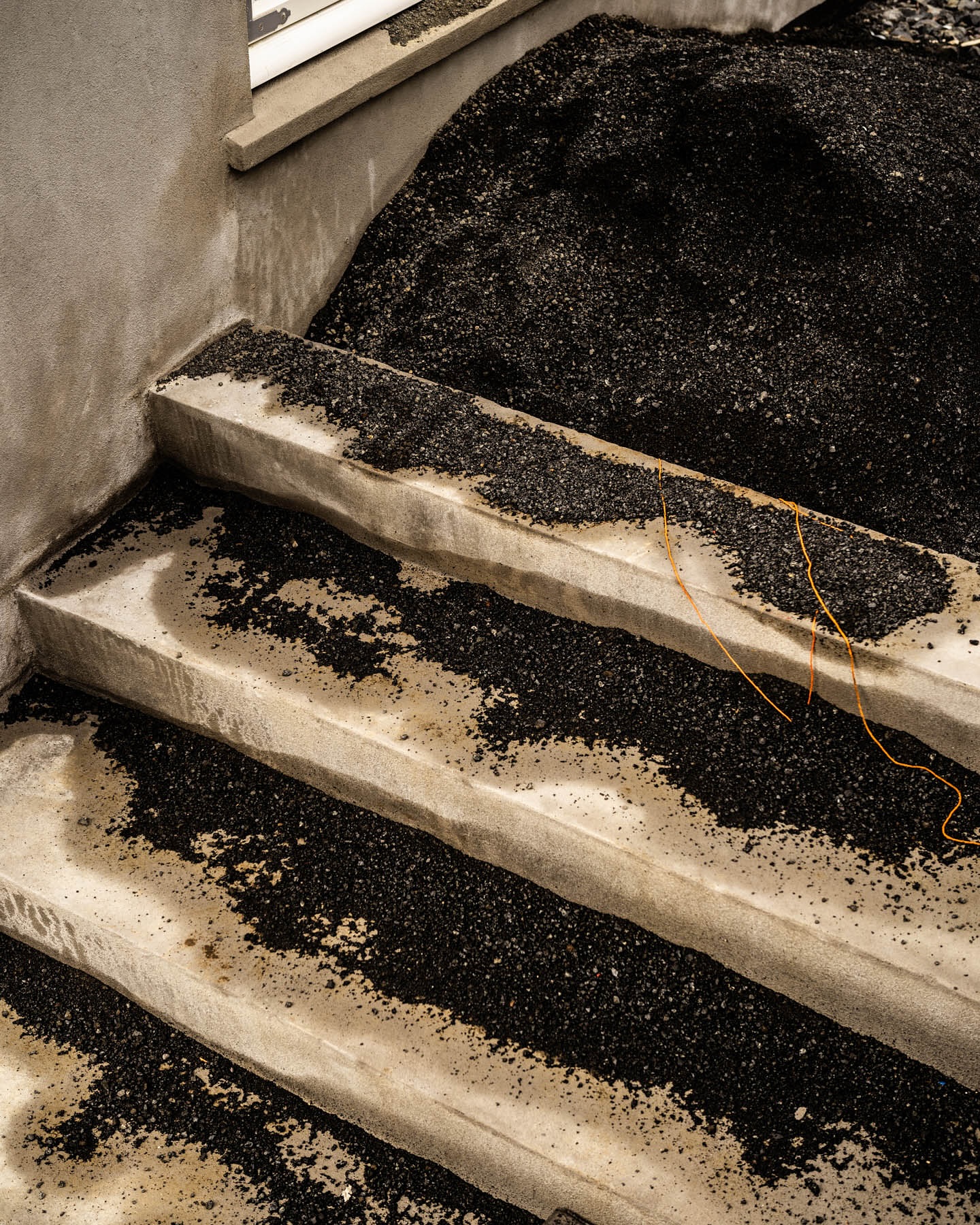 Concrete stairs covered with black granular material lead up to a window, creating an abstract, textured indoor scene.