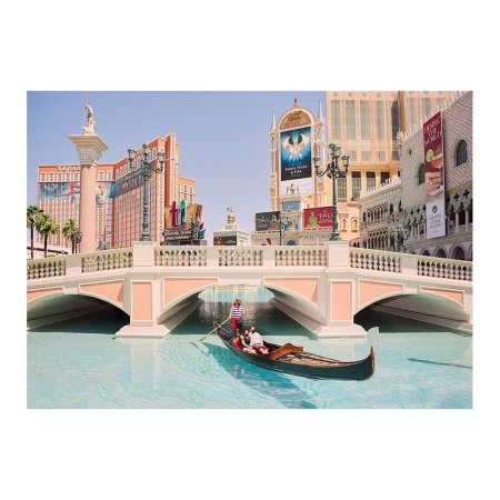 Gondola ride in a canal, tourists being rowed under an arched bridge in a replica Venice setting with Venetian-style buildings.