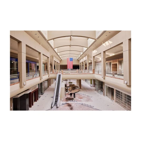 Interior of a mostly-empty two-story shopping mall featuring an escalator, overhead skylights, and a large American flag hanging overhead.