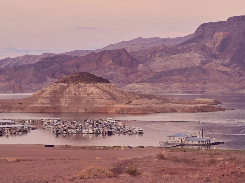 Scenic view of Lake Mead marina with houseboats, surrounded by desert mountains under a pastel sky at dawn or dusk.