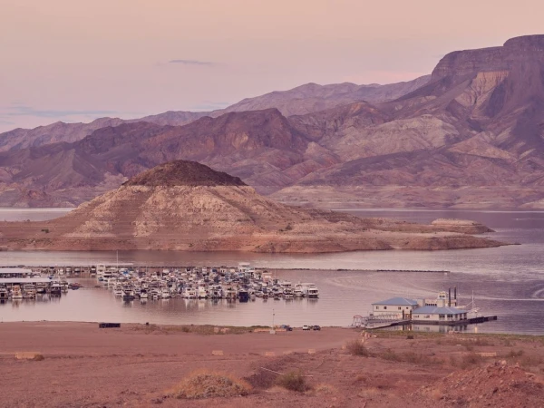 Scenic view of Lake Mead marina with houseboats, surrounded by desert mountains under a pastel sky at dawn or dusk.