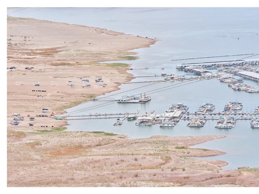 High-angle view of a marina on a partly dry lake, revealing arid shorelines, numerous boats docked, and vehicles near the shoreline.