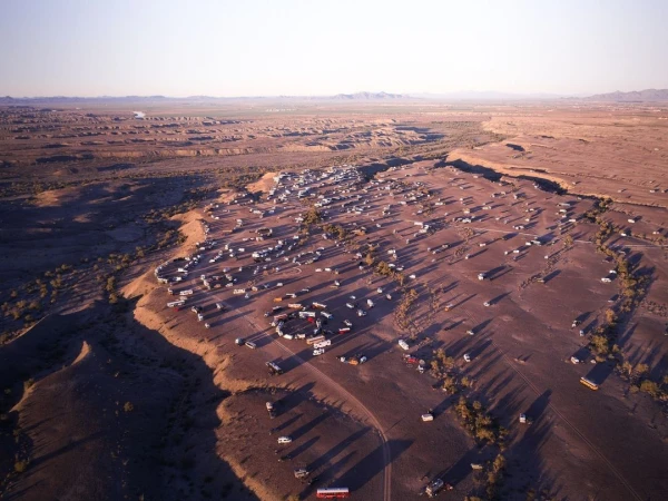 Aerial view of a large desert gathering with RVs and other vehicles, creating a circular formation, surrounded by arid landscape.