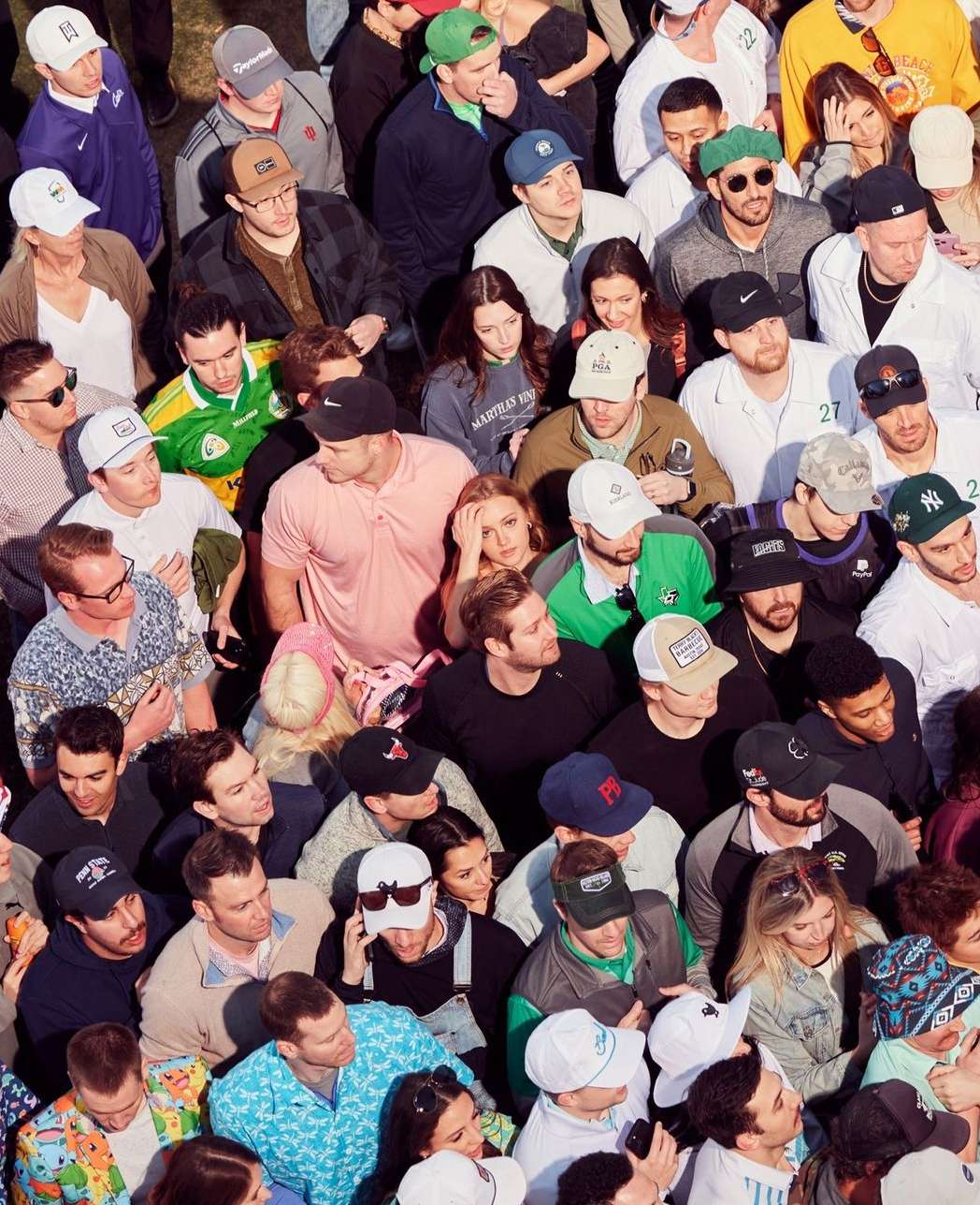 Aerial view of a large crowd of people gathered together, wearing various hats and clothing, suggesting a lively outdoor event or public gathering.