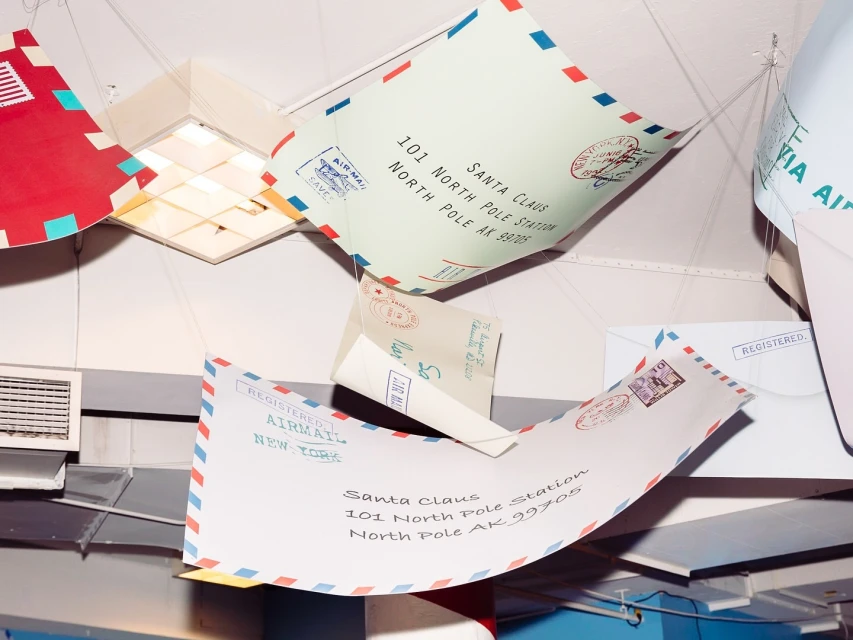 Envelopes addressed to Santa Claus are suspended from the ceiling, creating a whimsical and festive holiday display, evoking a sense of anticipation and joy.
