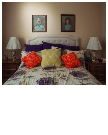 Bedroom interior featuring a bed with floral patterned bedding and pillows, two lamps on bedside tables, and portraits on the wall.