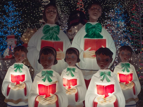 Christmas decoration with a choir of illuminated figurines in white robes holding red books and singing carols against a dark background.