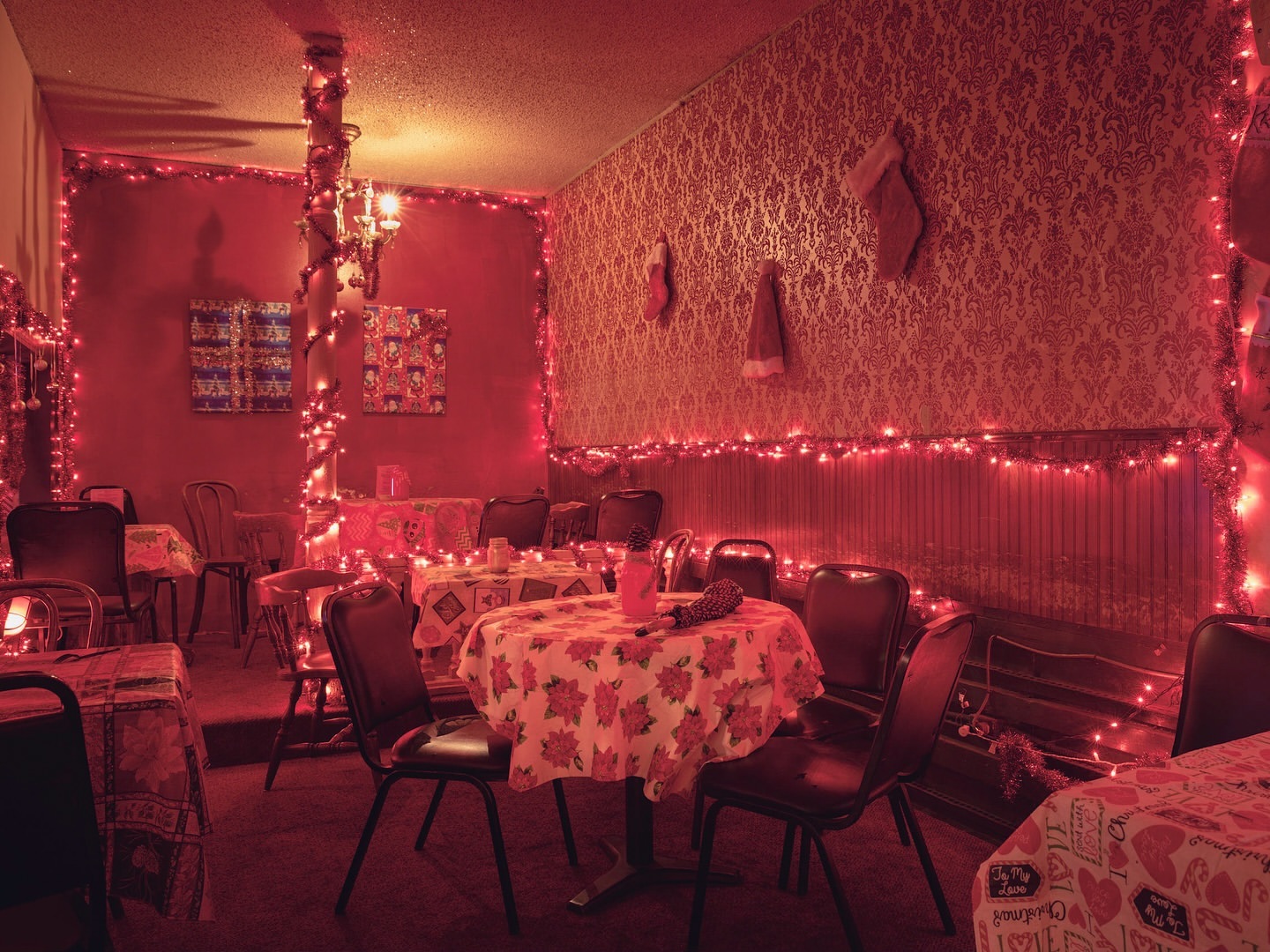 Interior of a restaurant or dining space decorated with red Christmas lights, patterned wallpaper, tablecloths, and vintage furniture creating a festive atmosphere.
