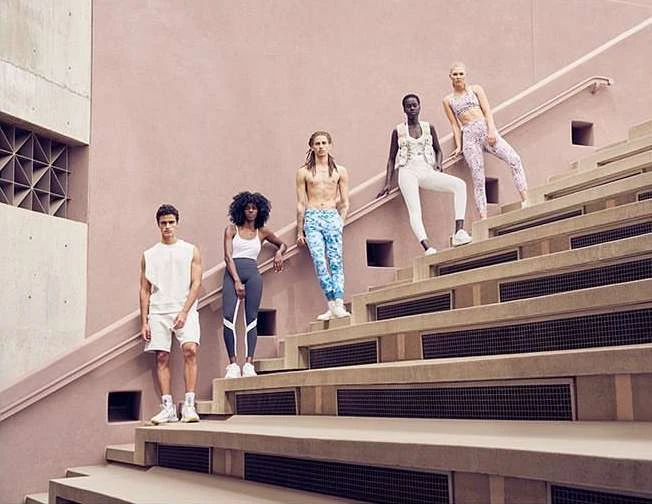 Five diverse models in athletic wear pose on tiered stairs against a light pink wall, creating a fashionable group shot.