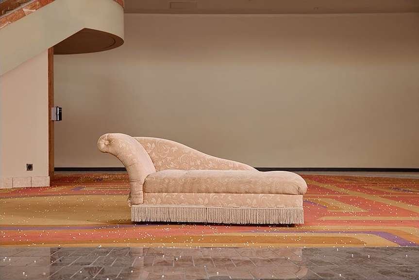 Vintage chaise lounge on patterned carpet in a room with pale peach walls and marble floor, evoking classic and architectural elements.