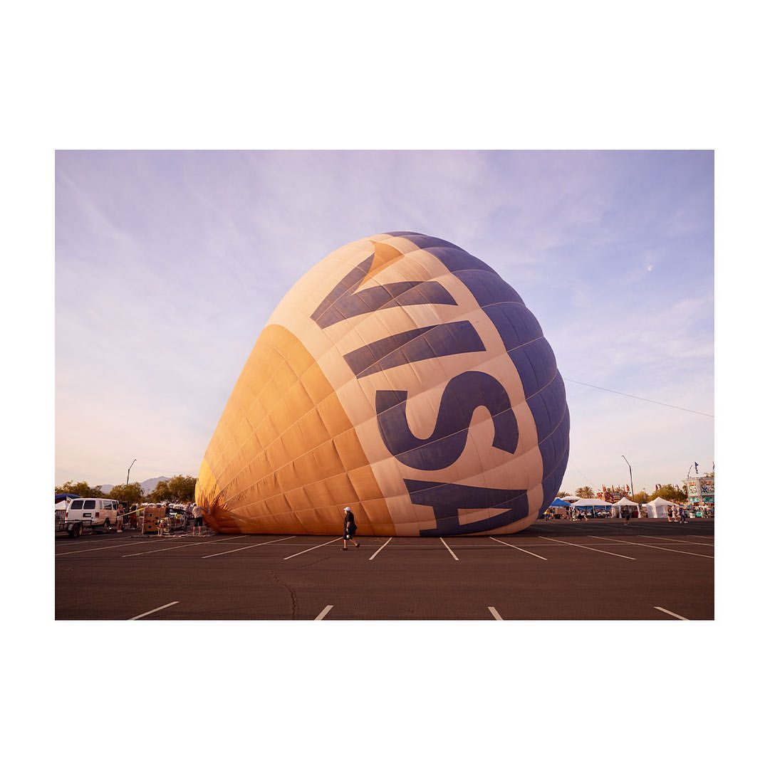 Large VISA-branded hot air balloon deflated in parking lot with a single person standing nearby, cars and tents visible in background.