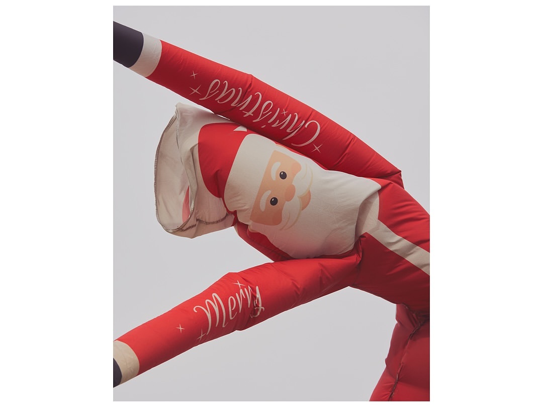 Inflatable Santa Claus figure against a neutral sky background, featuring Christmas and Merry text on its red and white design.
