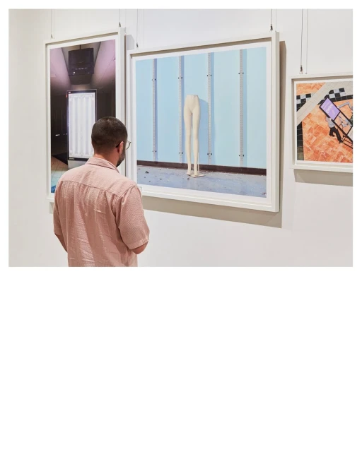Man with dark hair and glasses views photography in gallery, white frames, and light blue background, minimal composition, modern art museum.