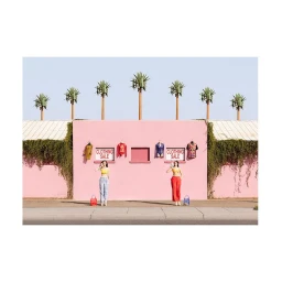 Two women posing in front of a bright pink building with clothing sale signs and palm trees under a clear blue sky