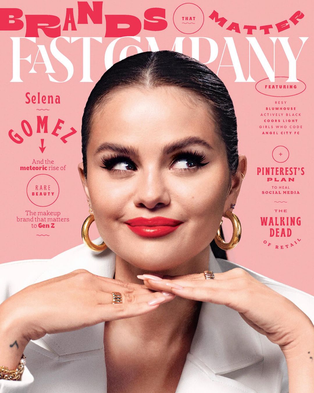 Magazine cover featuring Selena Gomez wearing a white blazer, gold hoop earrings, and red lipstick against a light pink background.