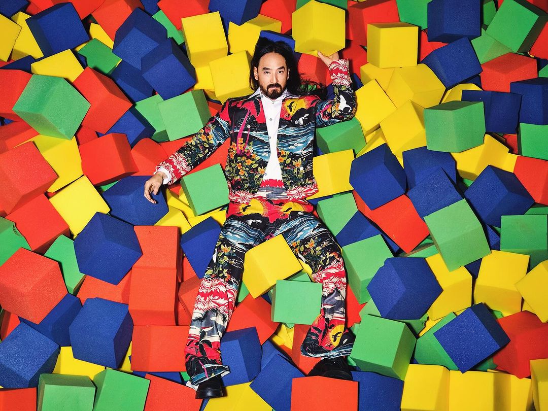 Adult male in a patterned suit surrounded by colorful foam cubes in a bright, indoor setting with a shallow depth of field.