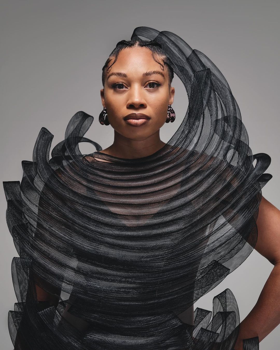 Elegant portrait of an adult woman with stylish braided hair and black couture fashion, posing against a neutral backdrop in a studio setting.