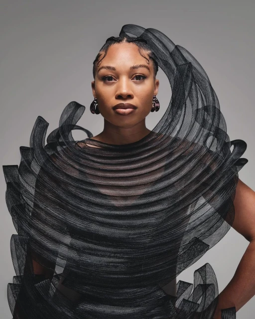 Elegant portrait of an adult woman with stylish braided hair and black couture fashion, posing against a neutral backdrop in a studio setting.