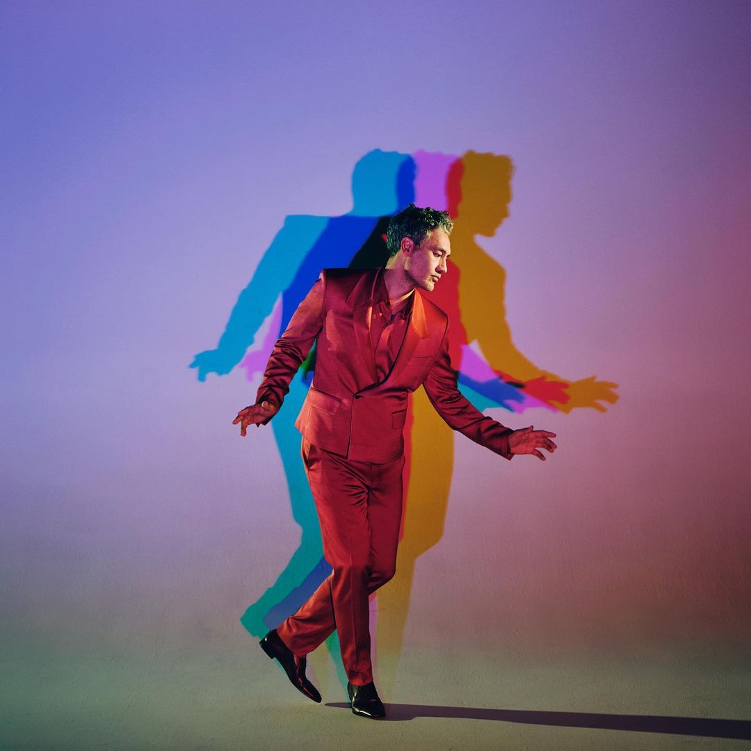 Young man in a red suit strikes a pose in a photo studio with colorful shadows adding depth and visual interest to the composition.
