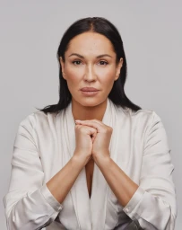 Portrait of a woman with dark hair wearing a white silk blouse against a neutral grey background, photographed by Jessica Chou.