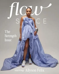 Allyson Felix standing in a blue strapless ruffled dress with a long train and white sneakers against a grey studio backdrop.