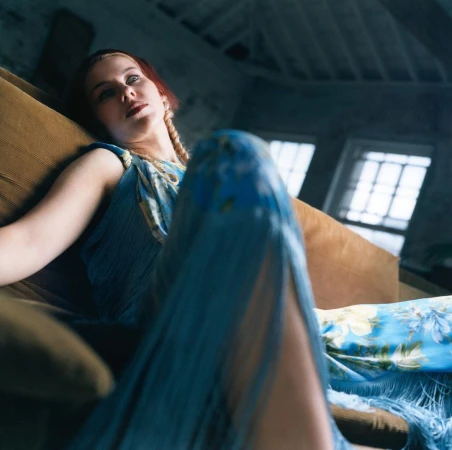 Woman in blue dress seated on a brown sofa, captured from a low angle with soft lighting.