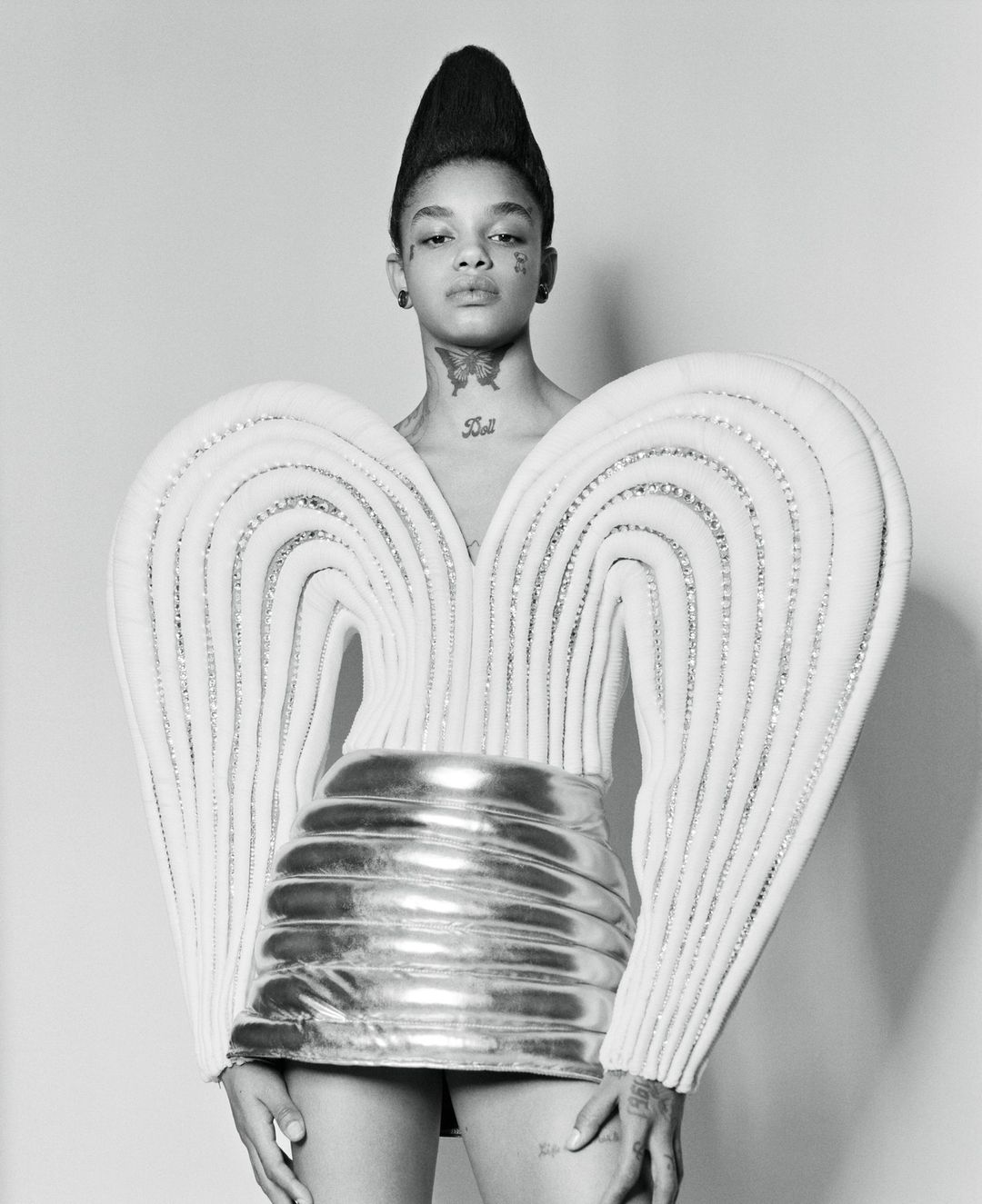 Portrait of a model wearing a sculptural white winged top and shiny metallic skirt with tall stylized hair by Jessica Madavo