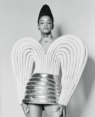 Portrait of a model wearing a sculptural white winged top and shiny metallic skirt with tall stylized hair by Jessica Madavo