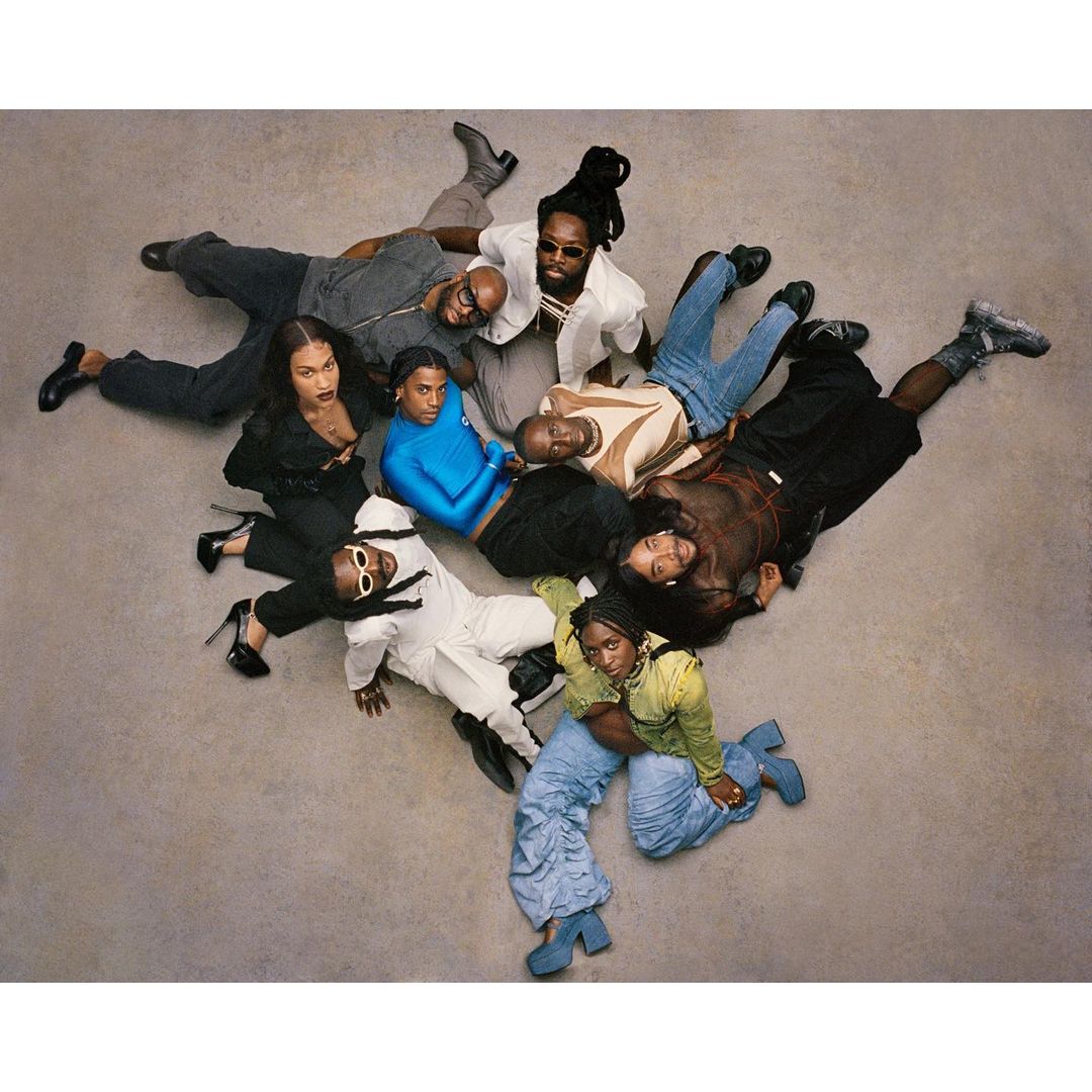 Eye-level shot of nine fashionably dressed adults lying on a seamless gray studio backdrop, featuring diverse attire and poses, shot in studio lighting.