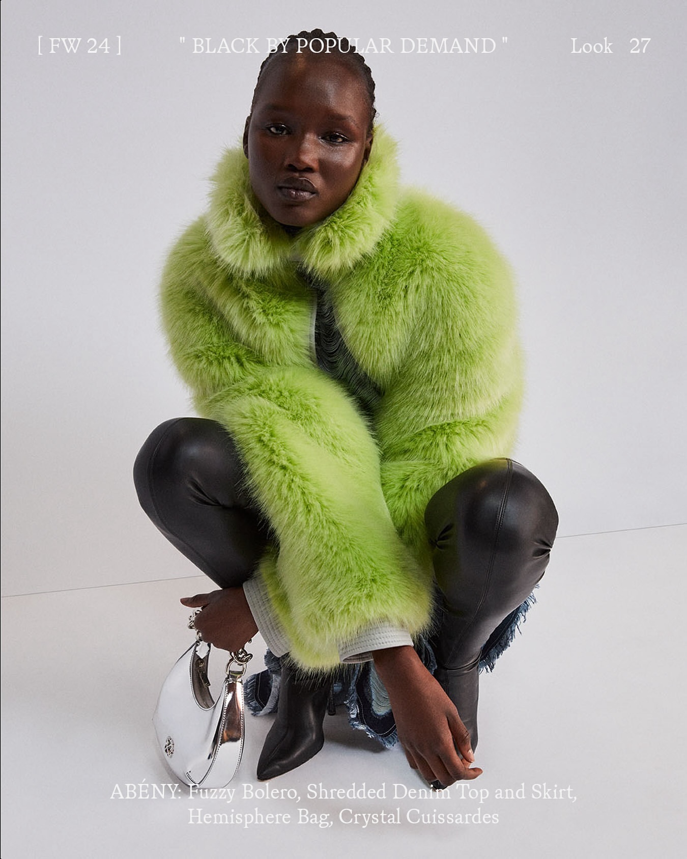 A model wears a vibrant chartreuse faux fur bolero, black leather pants, and pointy heeled ankle boots, holding a silver handbag in a studio.