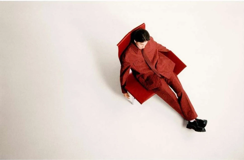 Overhead shot of a man in a patterned red suit lounging on a red chair against a bright white backdrop in a fashion editorial style.