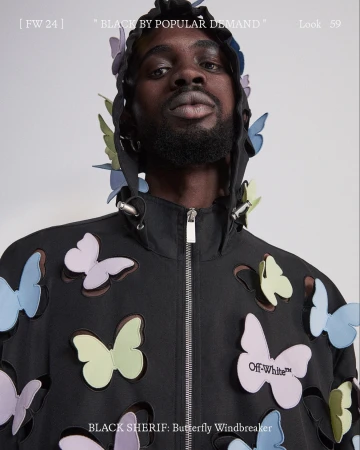 Black man wearing a black windbreaker embellished with multicolored pastel butterfly cutouts against a white background.