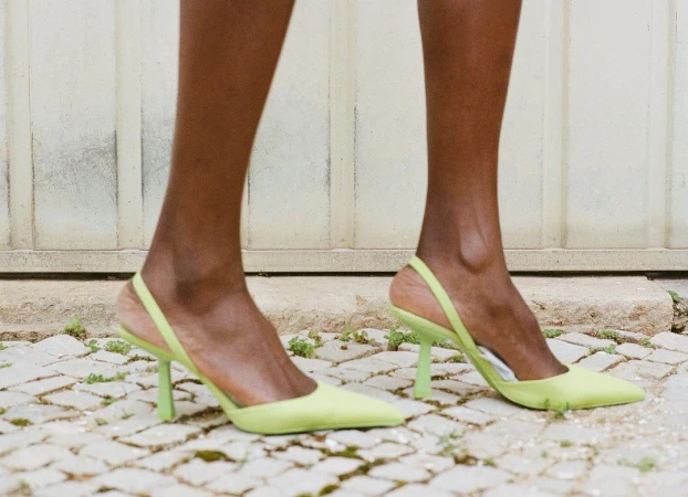 Close-up of an adult female model wearing light green slingback high heel shoes outdoors on a stone surface with a white door behind.