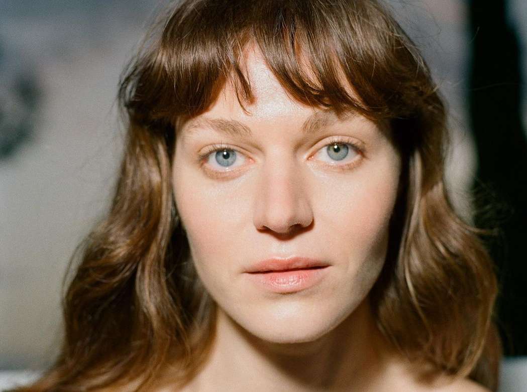 Close-up portrait of a woman with blue eyes, brown wavy hair with bangs, and neutral expression by Jessica Sidenros in Paris.